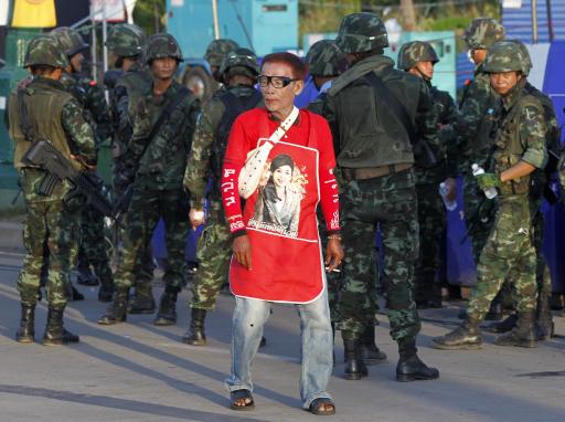 A member of the pro-government "red shirt" group walks past Thai soldiers at an encampment in Nakhon Pathom province on the outskirts of Bangkok