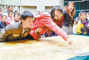 在哪兒?81位學童拼完長4公尺、寬108公分的《熊熊上河圖》拼圖，創作者莊信棠（下圖）出題目讓學童在圖中尋寶（右圖）。（陳俞霈攝）