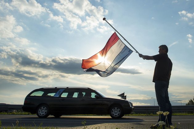Dutch Ronald Visee holds a Netherlands flag flying at half-mast (right) as a hearse carrying the remains of the victims of the Malaysia Airlines flight MH17 plane disaster are escorted on highway A27 near Nieuwegein by military police, on their way to bei