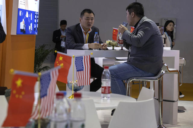 In this photo taken Wednesday, Nov. 6, 2019, visitors chat near American and Chinese flags displayed at a booth for an American company promoting environmental sensors during the China International Import Expo in Shanghai. Washington and Beijing have agreed to cancel tariff hikes as their trade negotiations progress, a Chinese Commerce Ministry spokesman said Thursday, Nov. 7, 2019. (AP Photo/Ng Han Guan)