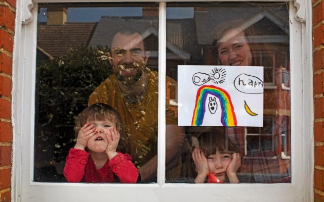 Amelie and her sister, Camille, look out from their front window in the COVID-19 coronavirus lockdown along with their parents, Victoria and Damian Kerr, in Berkhamsted, England - Lockdown saved no lives and may have cost them, Nobel Prize winner believes - AP