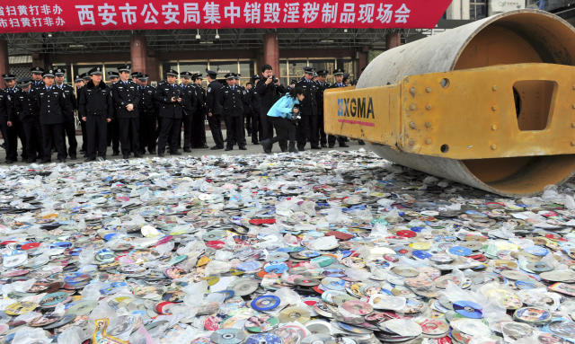 Police officers look on as a road roller is used to destroy confiscated pornographic DVDs and pirated publications in Xi'an, Shaanxi province March 17, 2011. Local police destroyed about 300,000 pornographic DVDs and pirated publications on Thursday during a campaign to stamp out porn and pirated products, local media reported. REUTERS/China Daily (CHINA - Tags: CRIME LAW MEDIA IMAGES OF THE DAY) CHINA OUT. NO COMMERCIAL OR EDITORIAL SALES IN CHINA